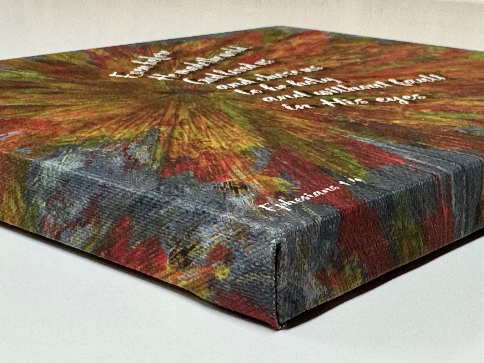 Side view of wrapped canvas showing vivid paint texture and scripture text from Ephesians 1:4