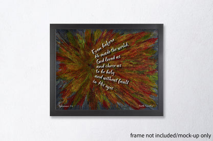 Vibrant scripture wall art framed in a sleek black frame against a white wall. The text reads 'Even before He made the world, God loved us...' from Ephesians 1:4. Frame not included.